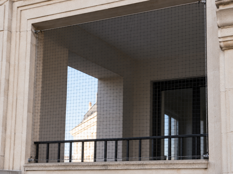 Filet anti-pigeon noir tendu sur câble inox périphérique fermant une loggia d'immeuble
